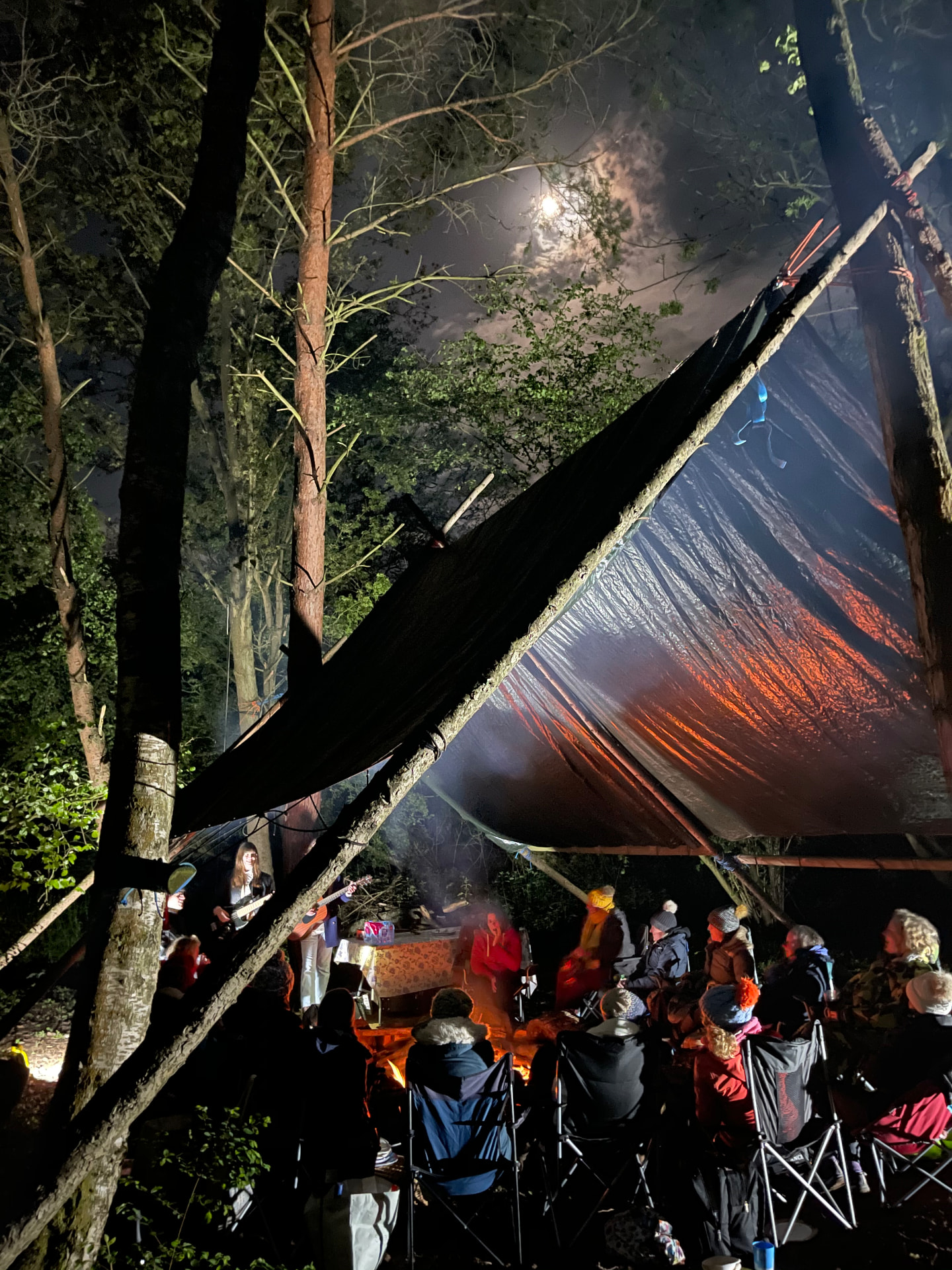 Evening musical performance and gathering around the fire under tarp shelters at Viking Camp, Buckland Park