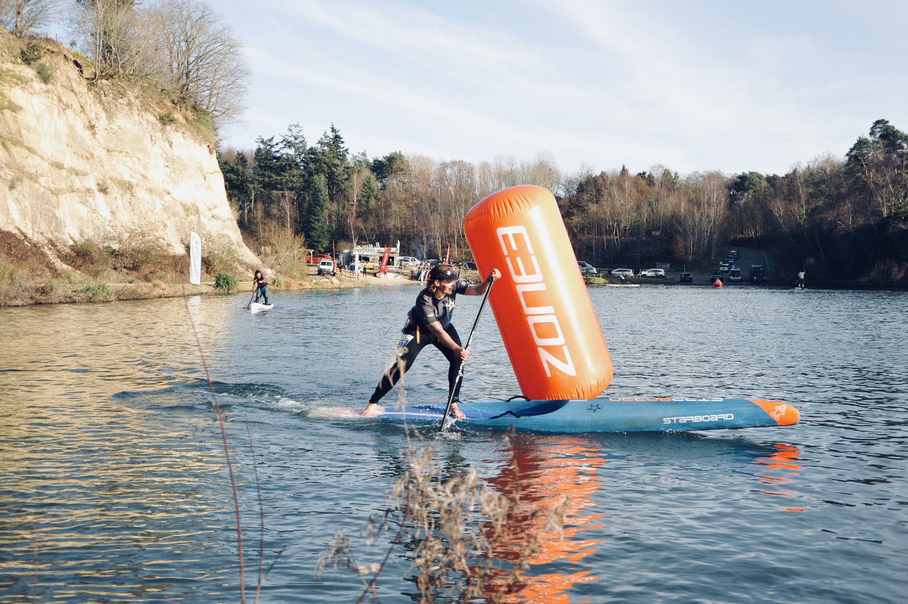 A paddler in a wetsuit turning tightly around an inflatable orange marker buoy on a winter lake at GLAGLA UK