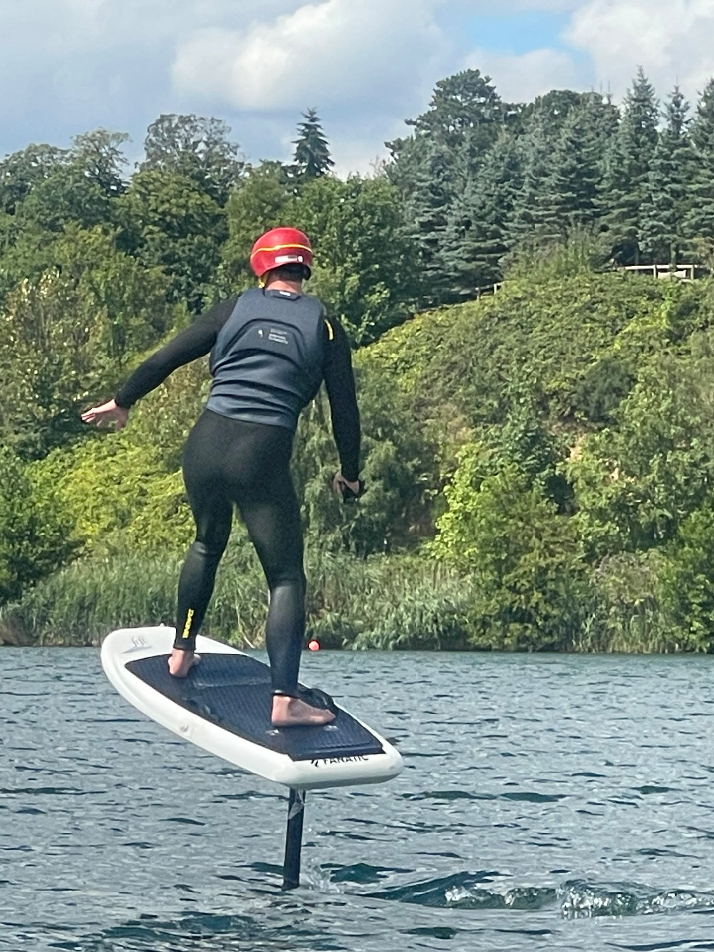 An e-foil rider in a red helmet flying the board clear of the water in a controlled stance, the full foil mast visible below the board at Buckland Park Lake