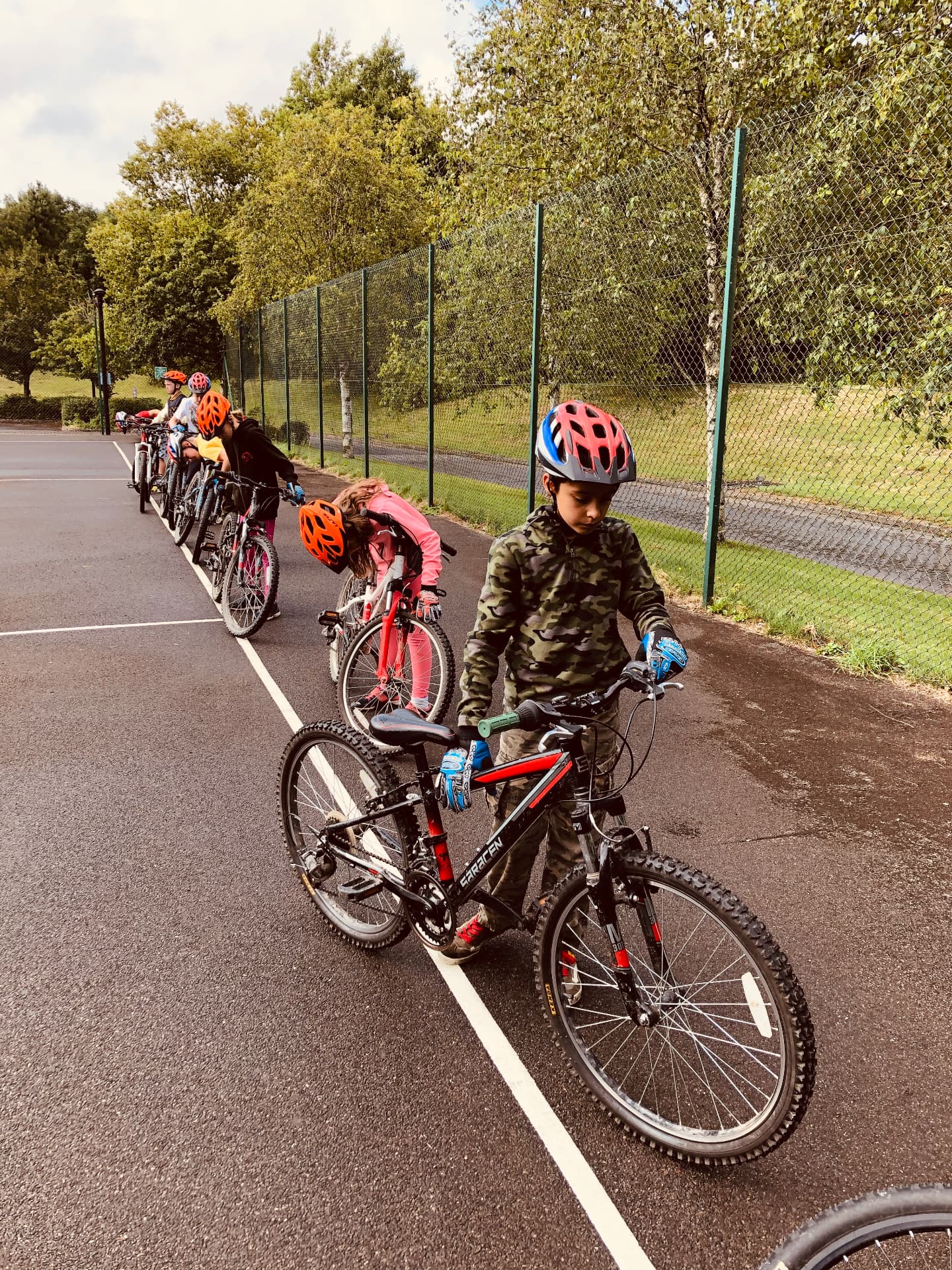 A line of young riders standing beside their mountain bikes on tarmac, checking their bikes before a session