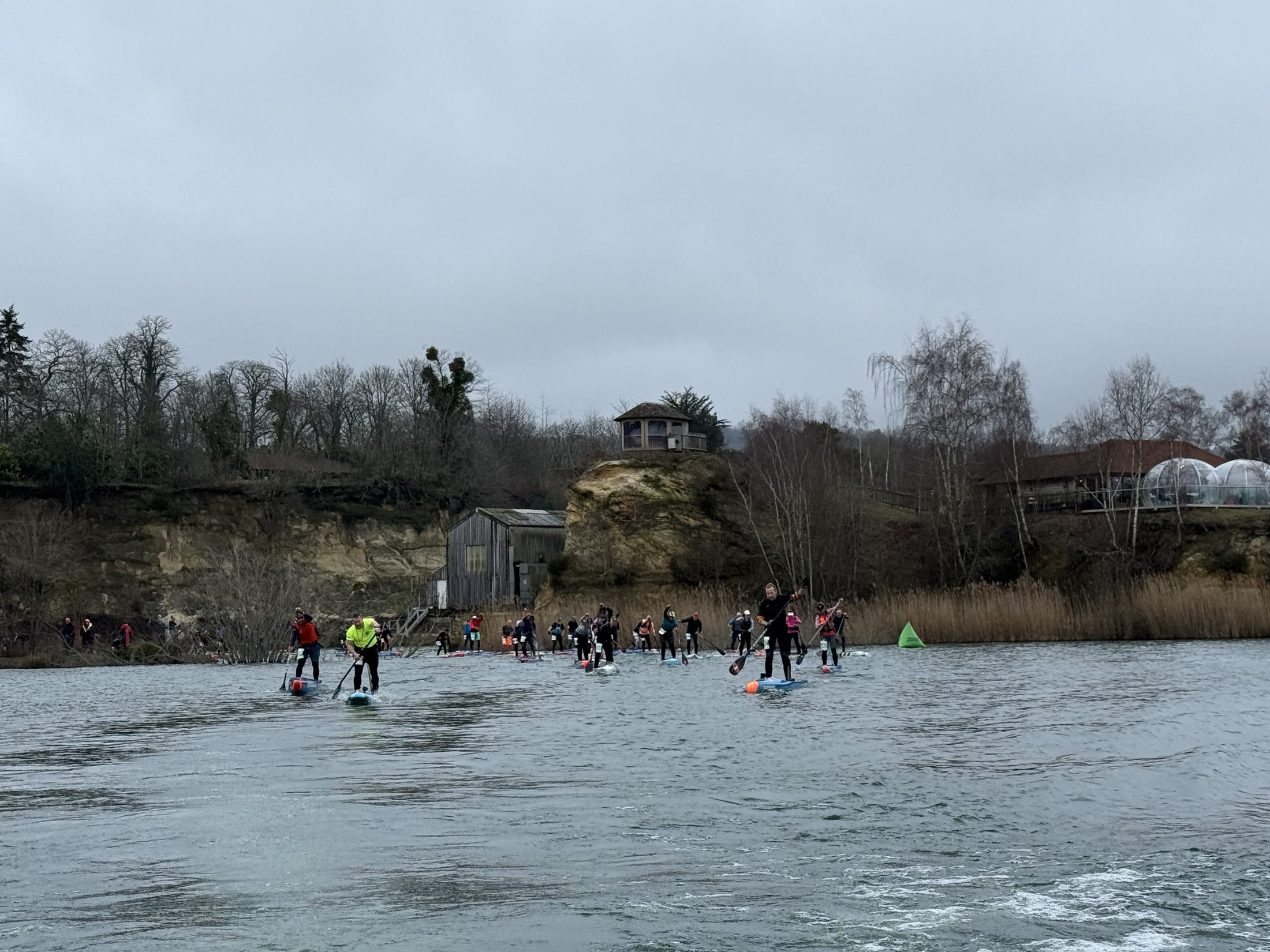 A long line of paddlers strung out across the winter lake in front of the quarry cliffs at GLAGLA UK