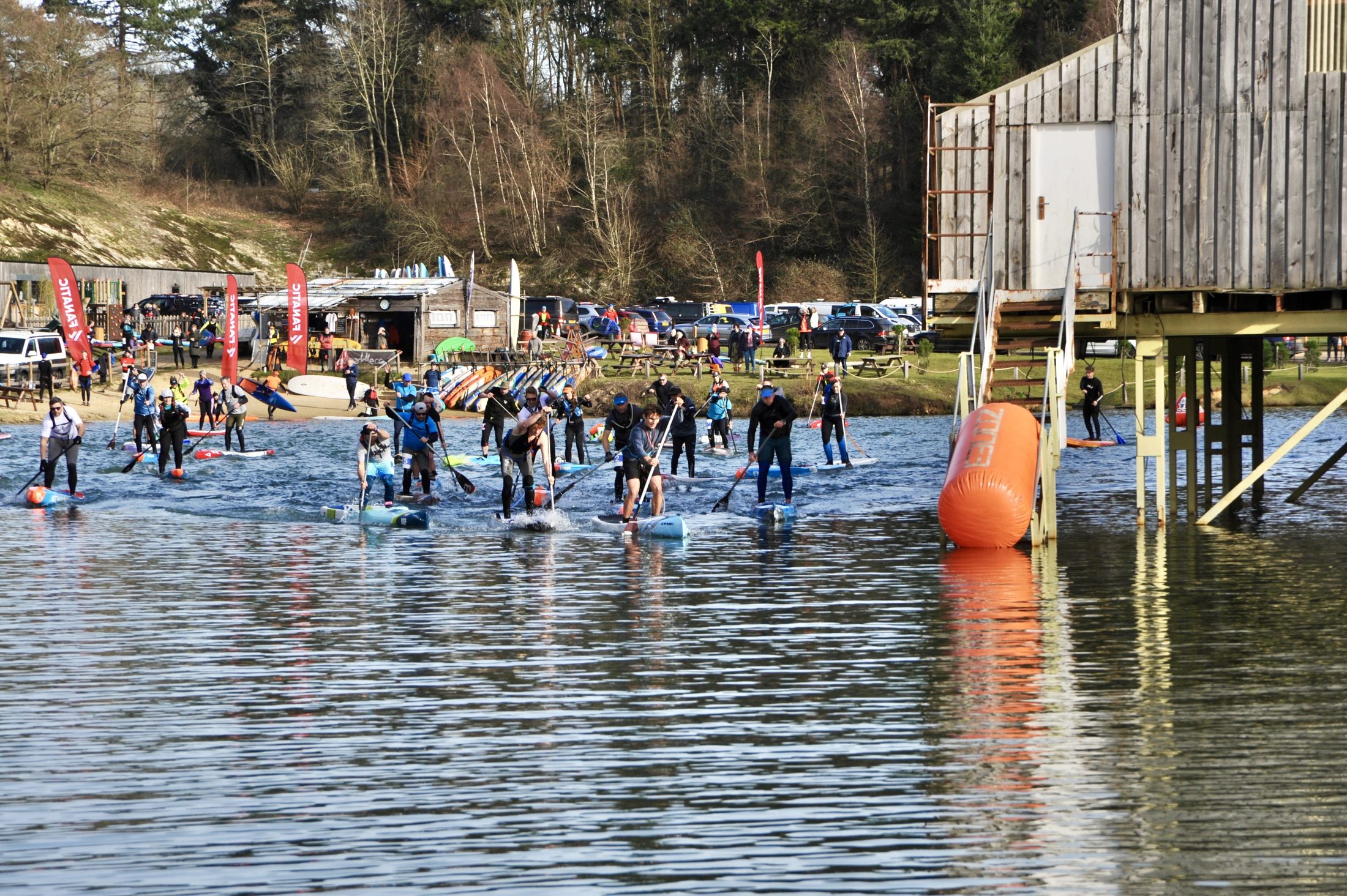 A large group of paddlers on race boards heading out past the marker buoy and event flags at GLAGLA UK