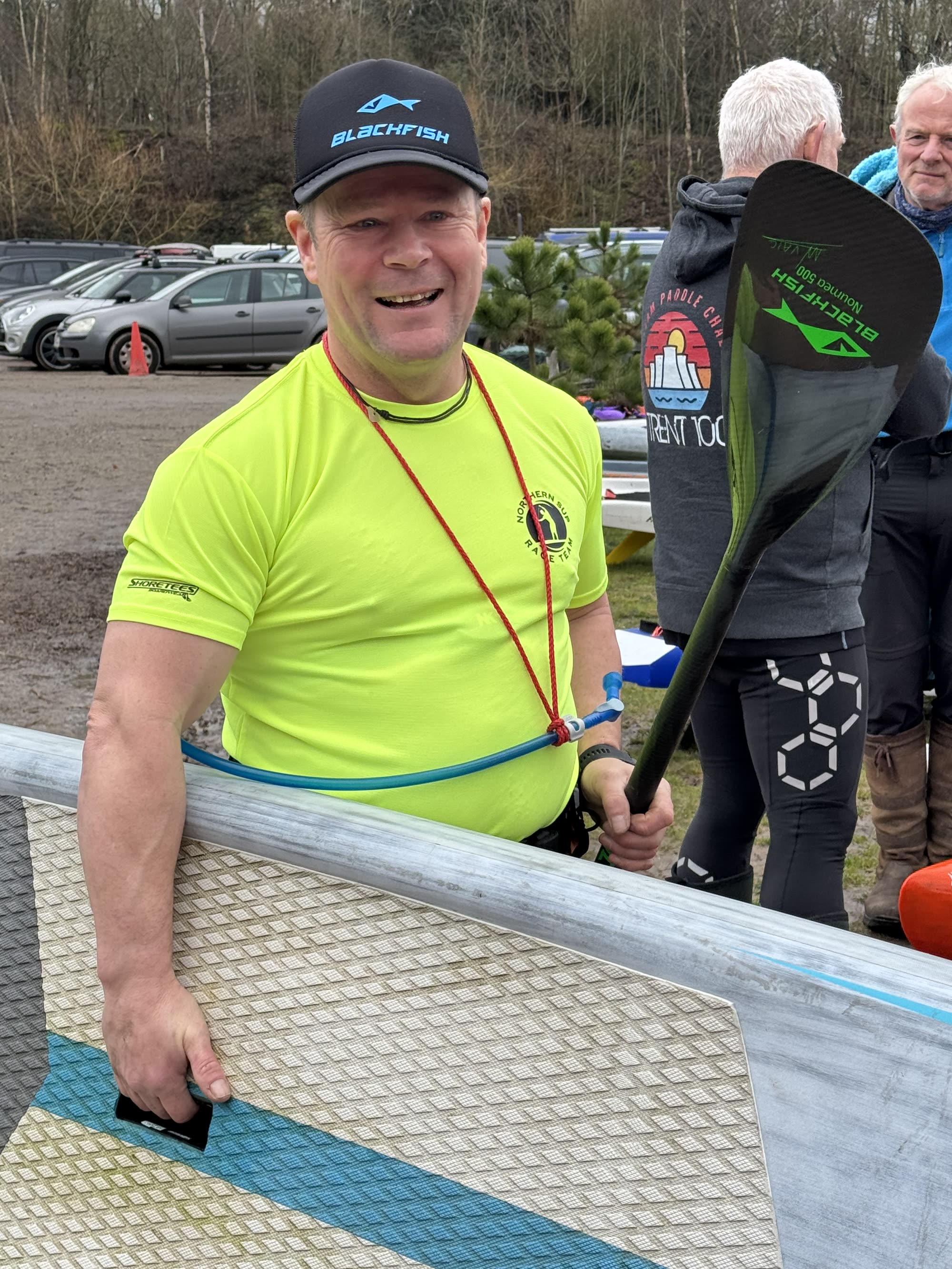 A grinning racer holding his paddle and race board in the event car park at GLAGLA UK