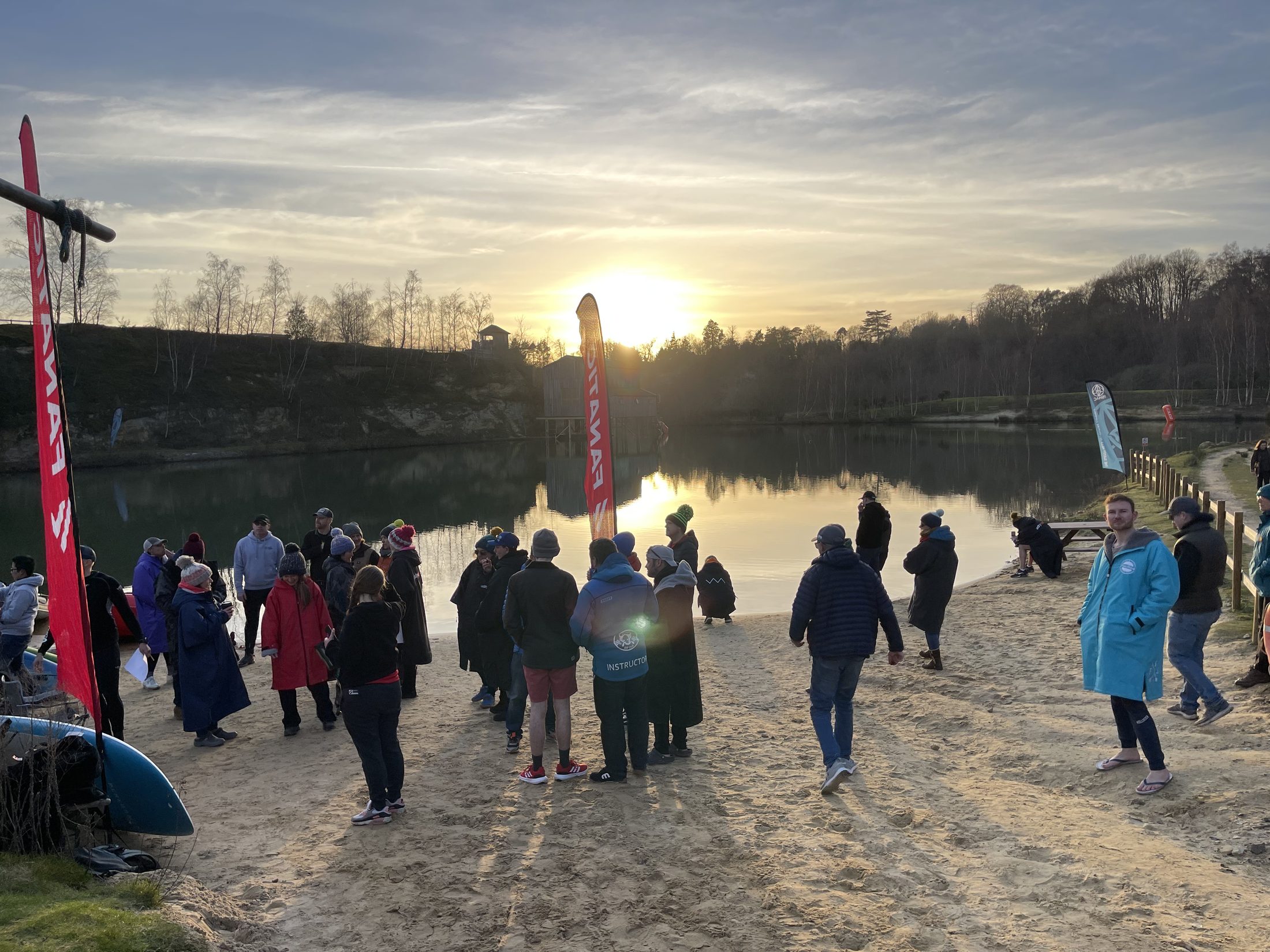 Paddlers and supporters gathered on the beach in winter kit as the sun sets over the lake at GLAGLA UK